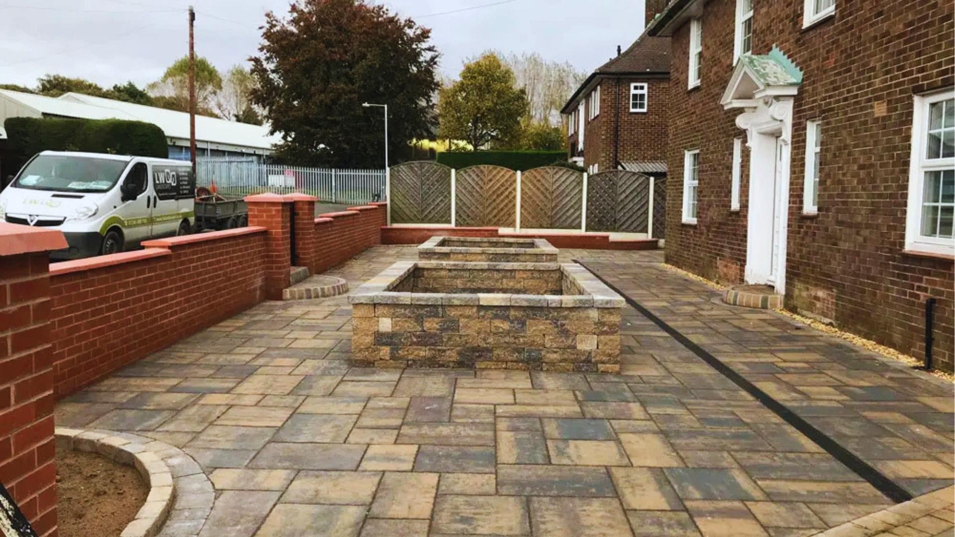 Newly paved stone driveway with raised brick planters sits beside red brick home and white van, showing shared access potential.
