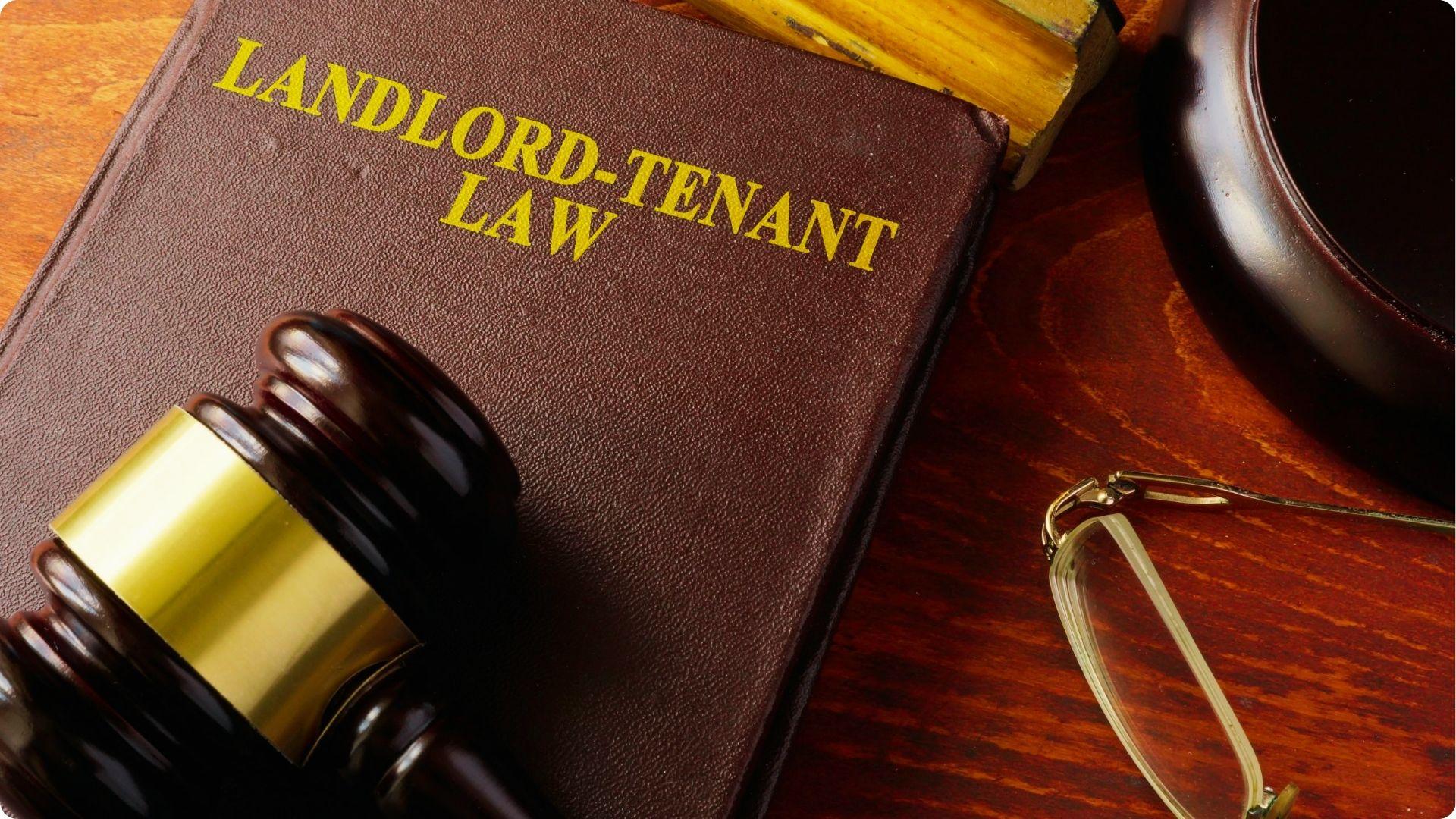 Gavel resting on a "Landlord-Tenant Law" book beside reading glasses on a desk.