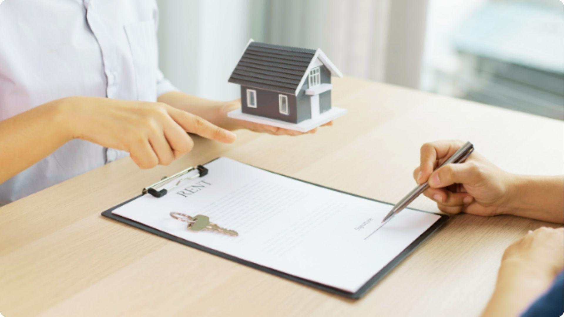 One person holds a house model while another signs a document labeled RENT on a clipboard.