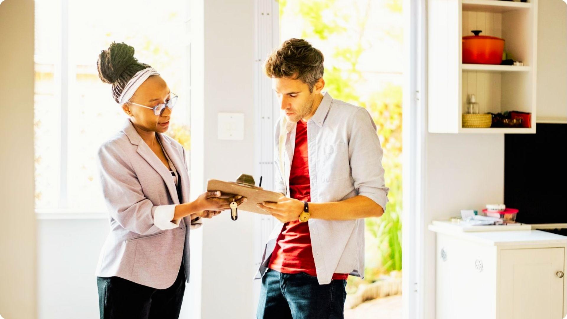 A real estate agent hands house keys to a buyer while reviewing paperwork in a sunlit home.