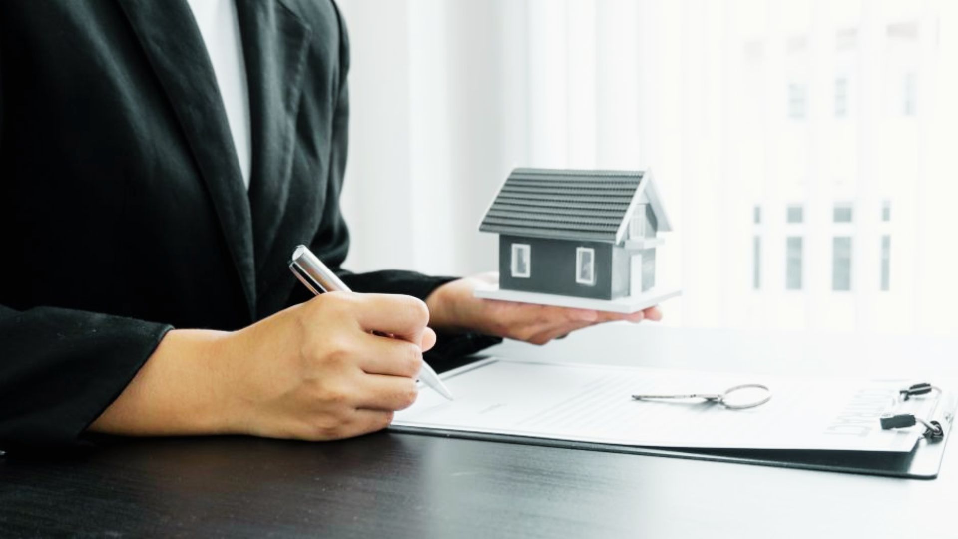 A woman in a business suit signs a contract with a house model beside her, highlighting property trust considerations.