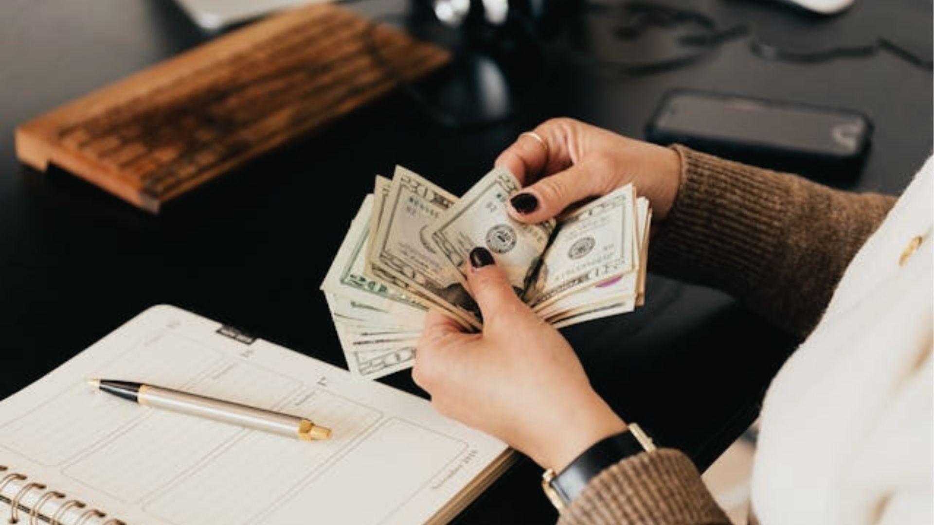 Hands counting cash over planner and pen on desk, showing budgeting for living trust cost setup.