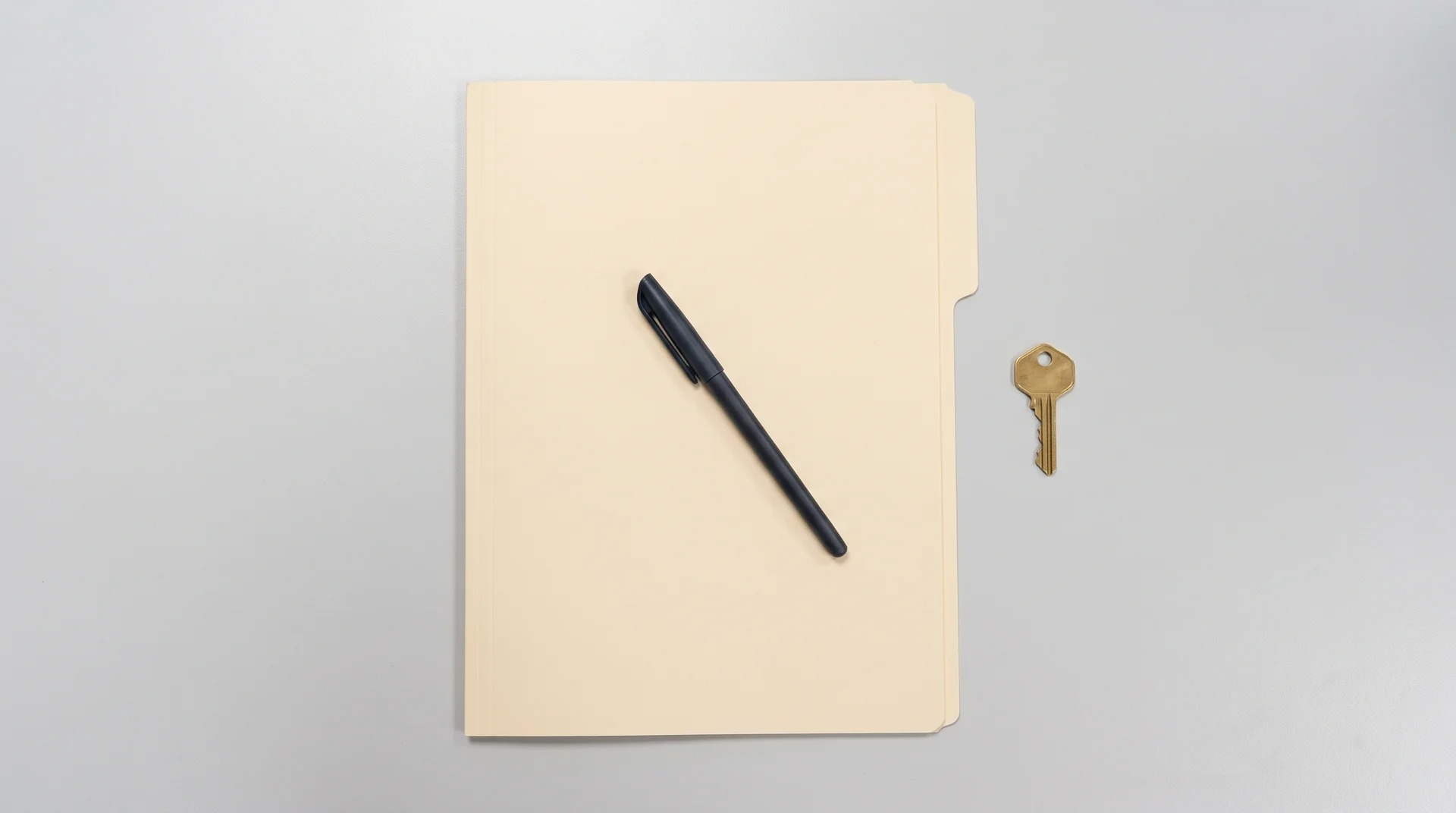 A closed folder with a pen and a house key resting on a desk