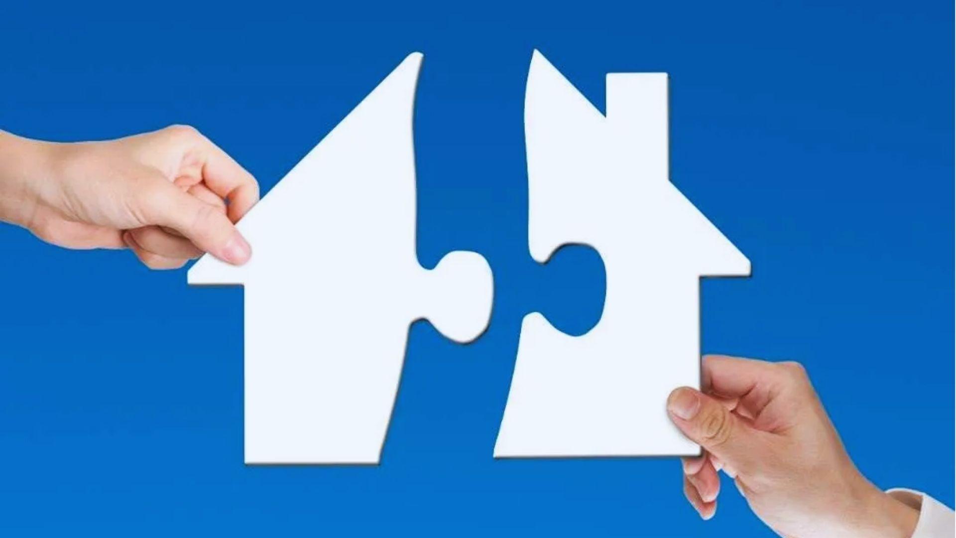 Two hands holding white house-shaped puzzle pieces about to connect against a solid blue background.