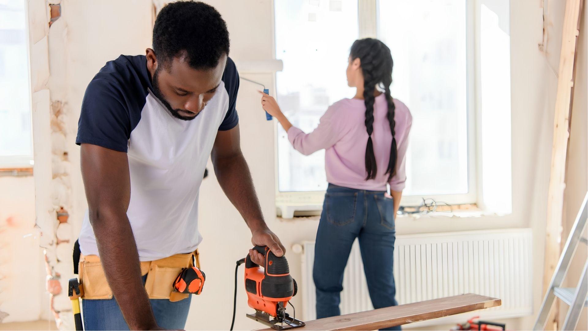 Couple renovating a home with power tools and painting interior walls together.