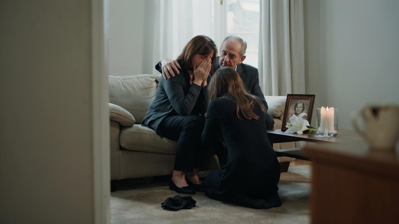Family comforts crying woman on couch near photo and lit candles.