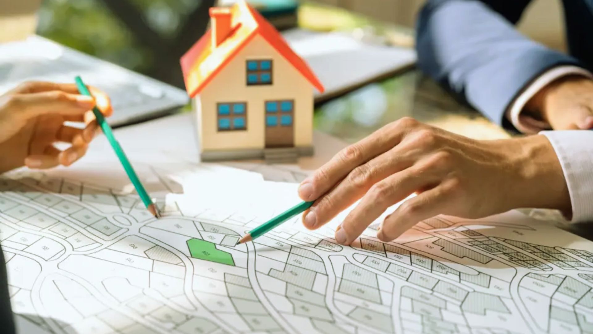 Real estate agents pointing at green plot on housing site plan map with model house, property investment planning