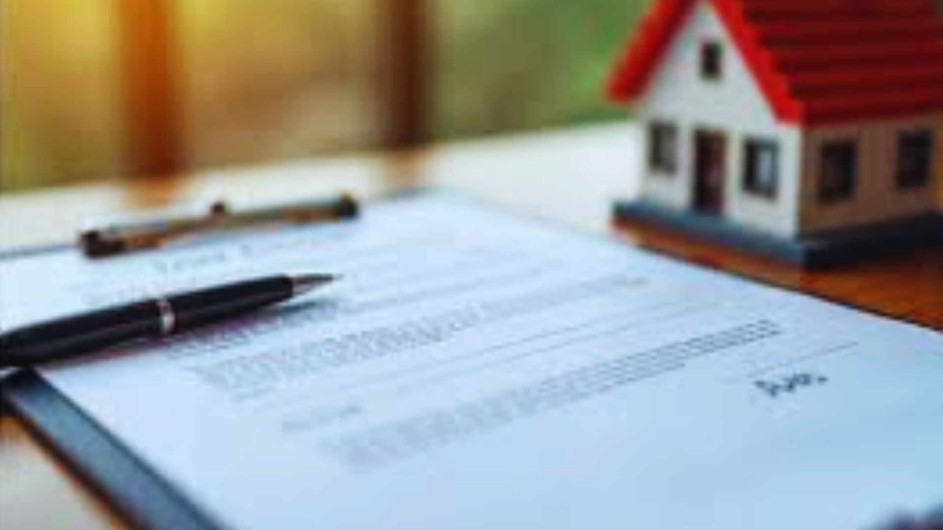 A pen rests on a signed paper on a clipboard near a small toy house.
