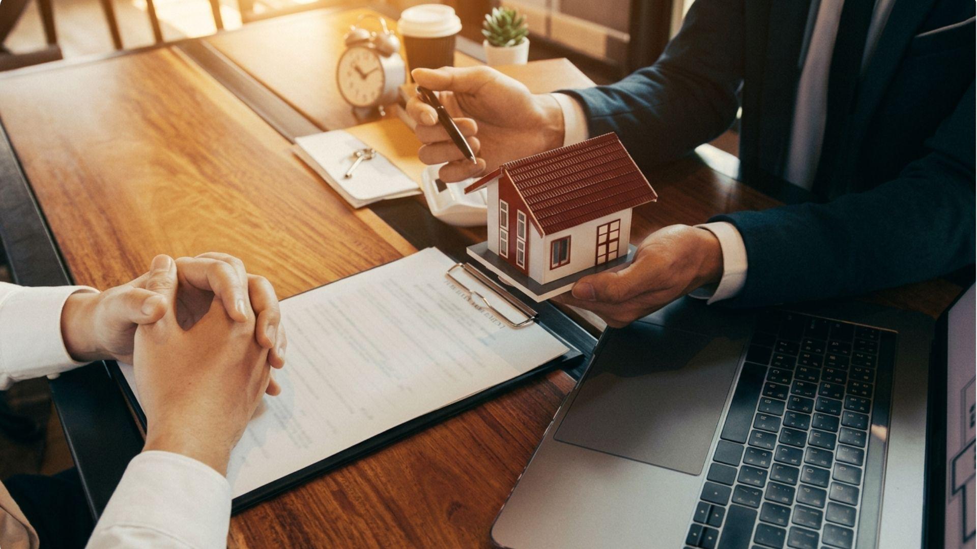 Real estate agent presenting model house to client reviewing contract with laptop.