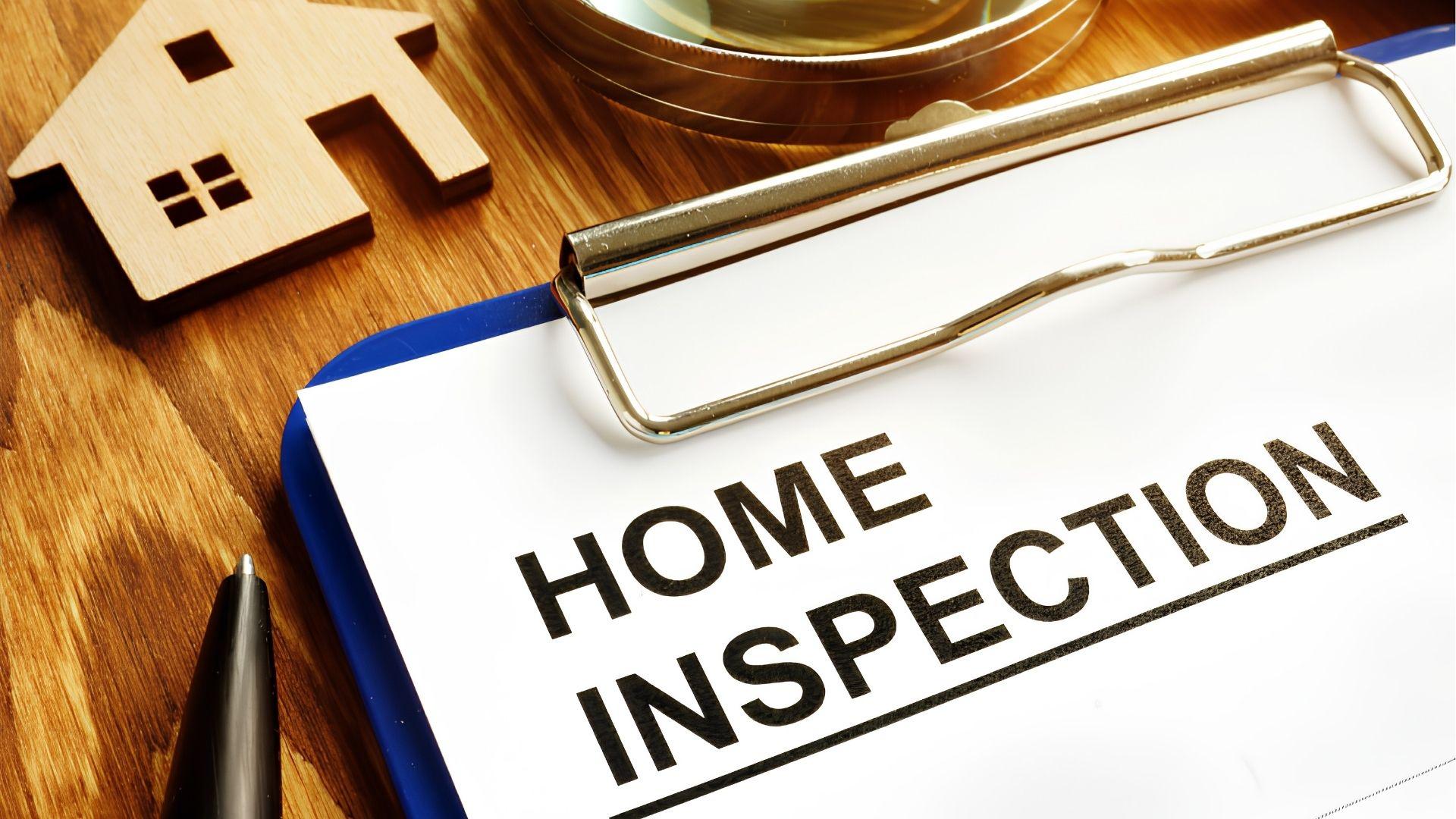 Home inspection clipboard beside wooden house model and magnifying glass