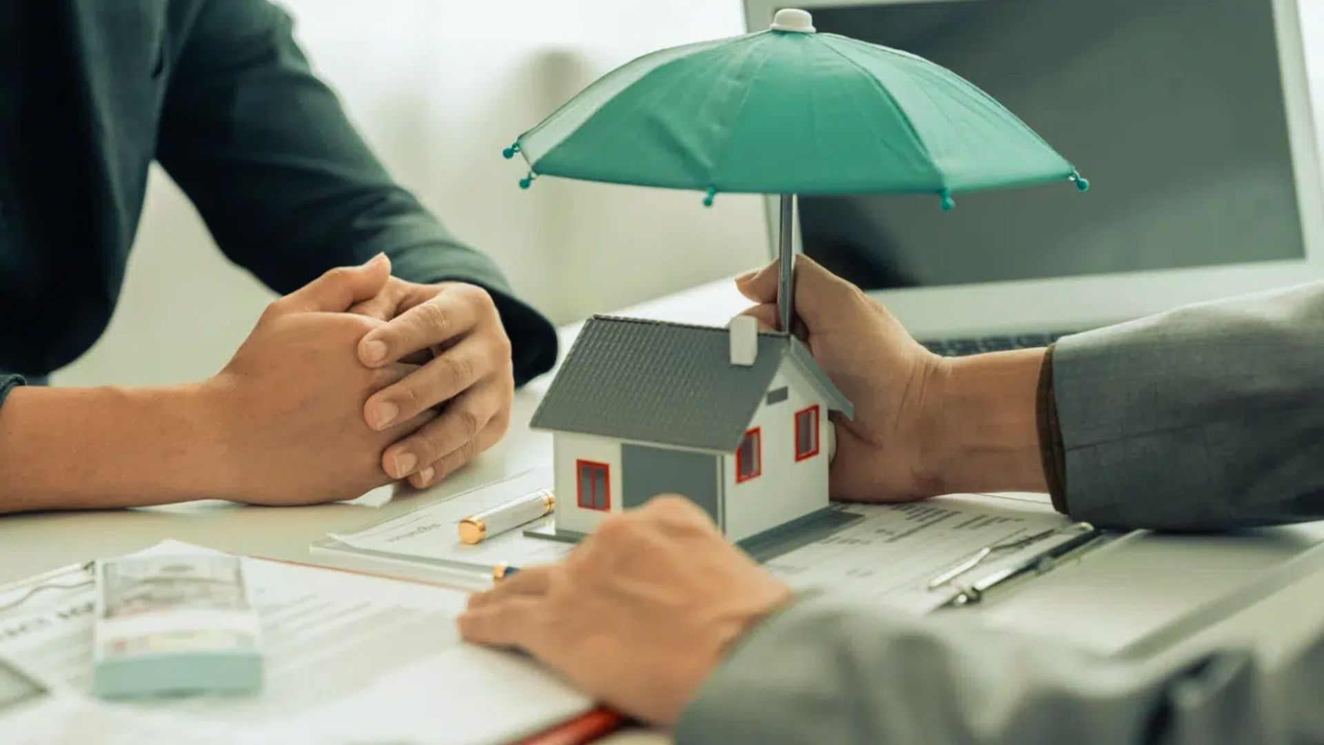 Home insurance protection concept with model house under umbrella, agent and client meeting