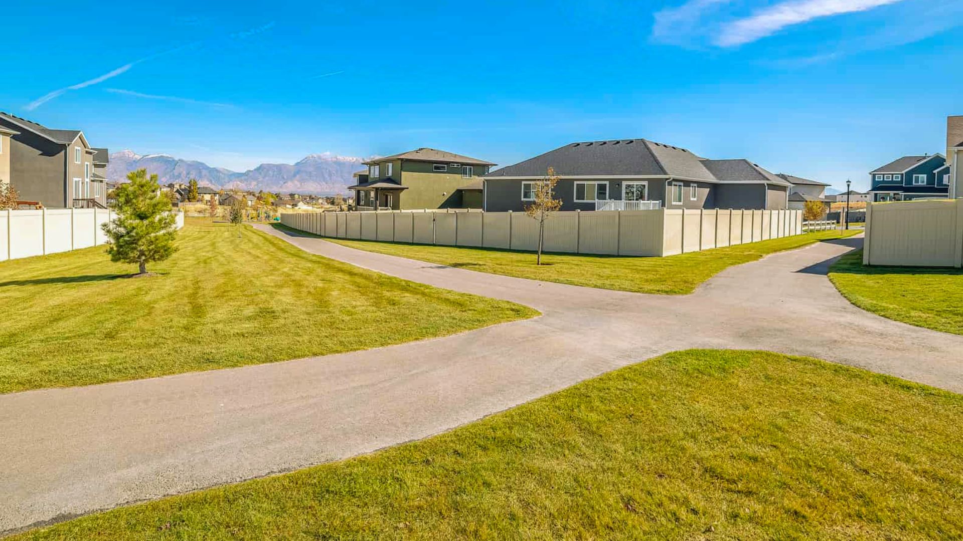 Paved shared access trail easement between fenced suburban homes with green lawns and mountain views