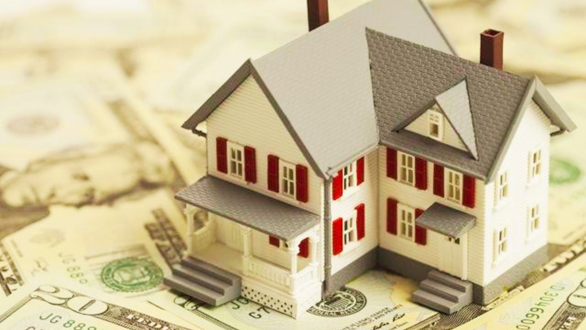 A miniature house atop a pile of cash, representing the costs and benefits of reverse mortgages.