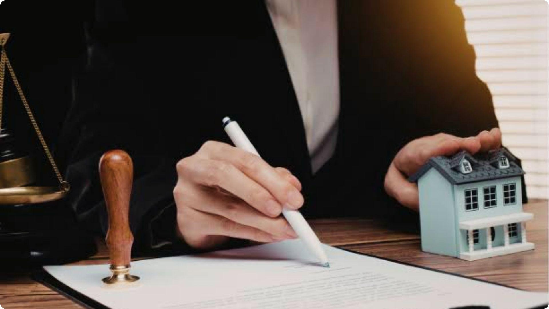Lawyer signing real estate deed transfer documents with house model and notary stamp on desk