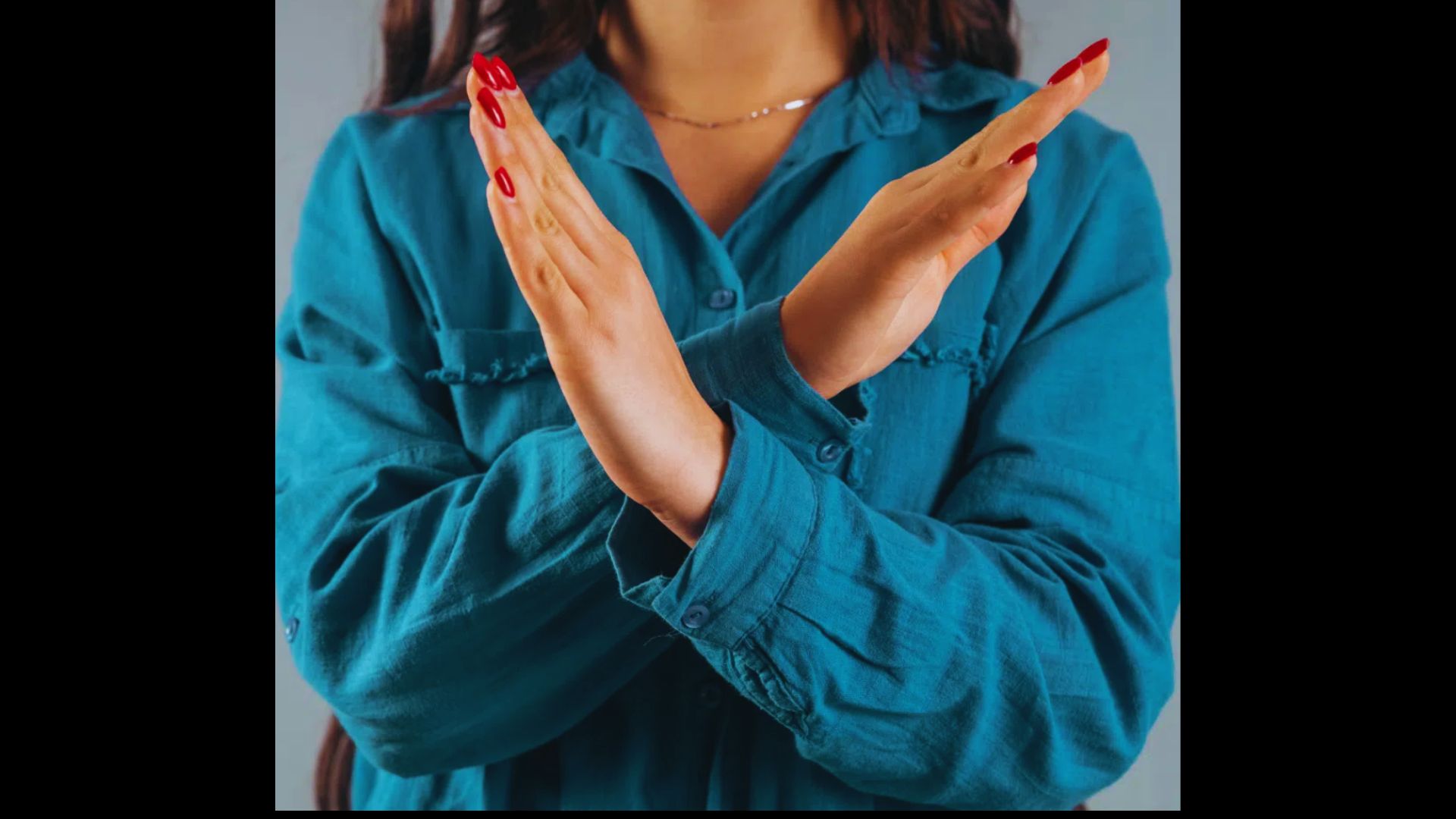 Woman in a blue shirt making a stop gesture with crossed hands.