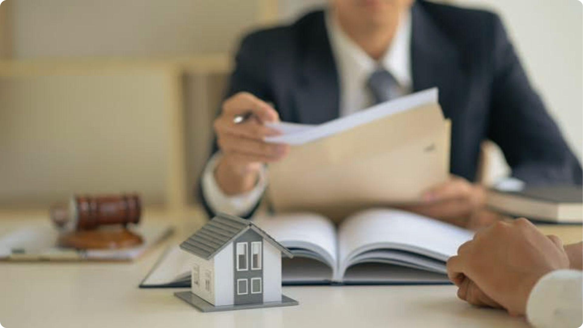 Lawyer reviewing legal files with client across table displaying house model and gavel for property dispute consultation.