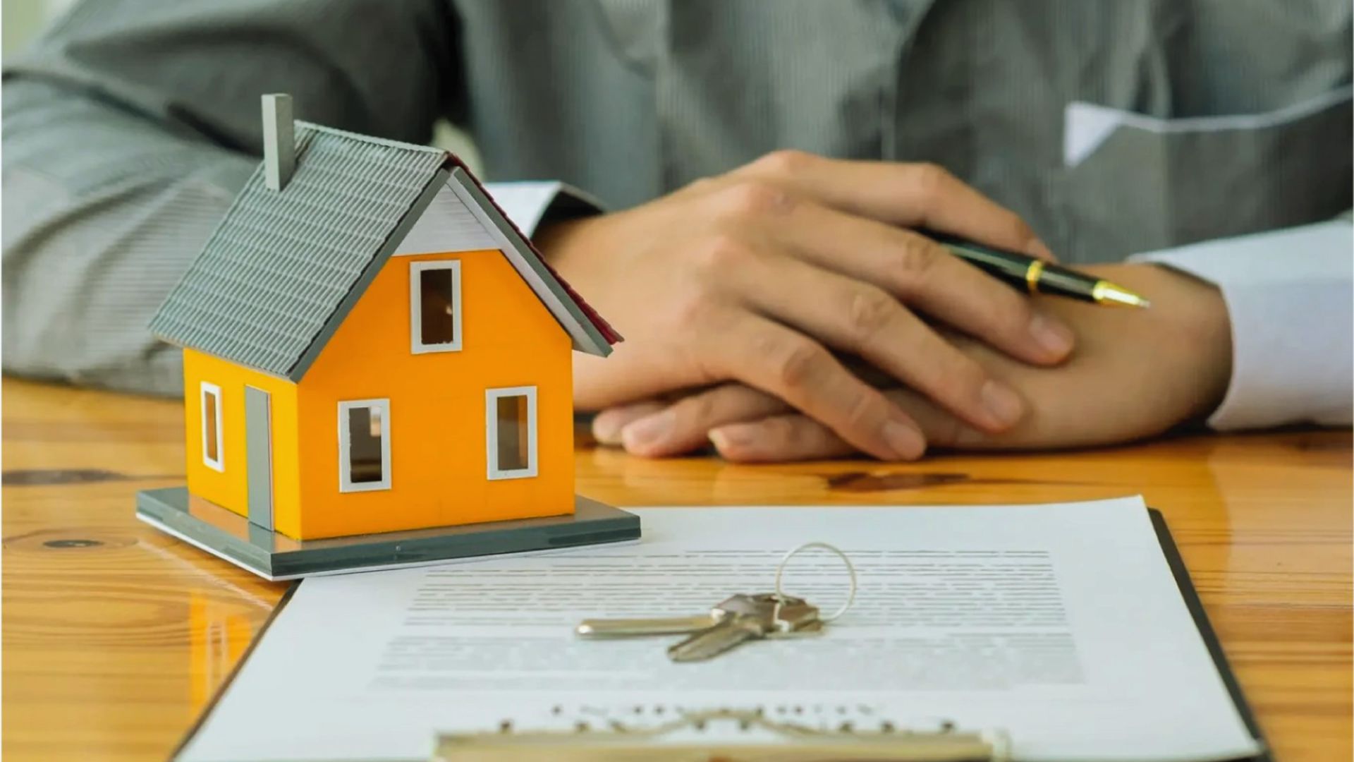 Orange miniature house model with keys on property contract, home loan closing and real estate deed signing