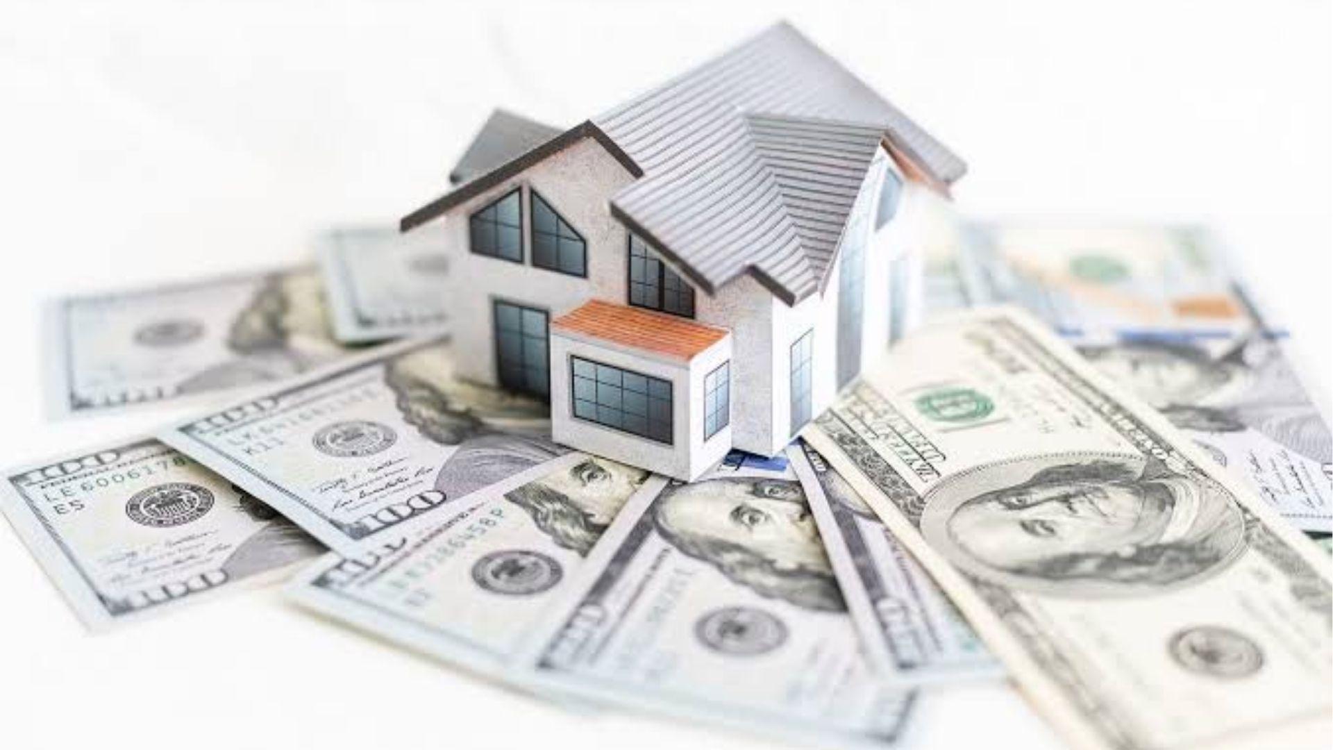 Model house placed on U.S. dollar bills representing real estate costs.