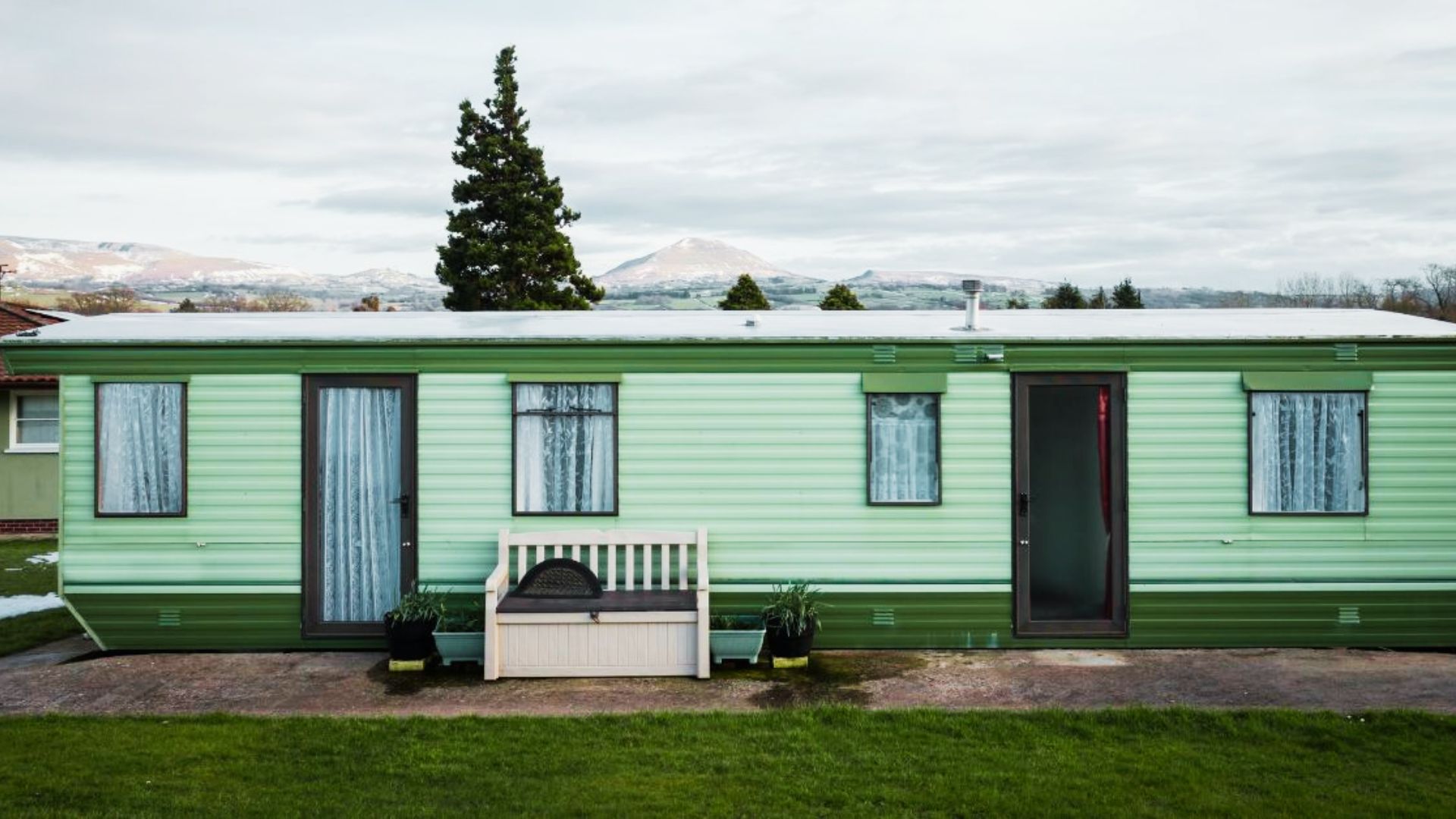 A green mobile home with a bench in front, illustrating a potential living space for eligible residents.