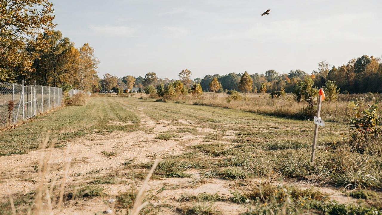 Empty ground lot with marker sign, fence, and autumn trees nearby.