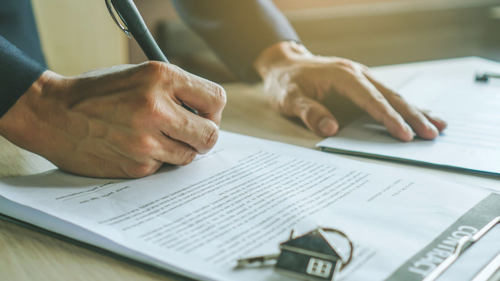 Close-up of hands signing home purchase agreement contract with house key during closing