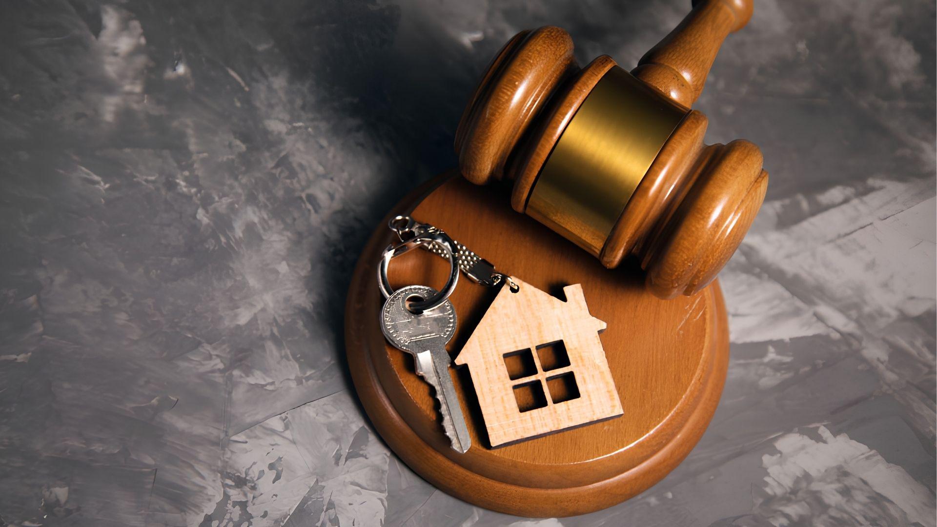 Wooden gavel with a house keychain and key on a gray textured surface