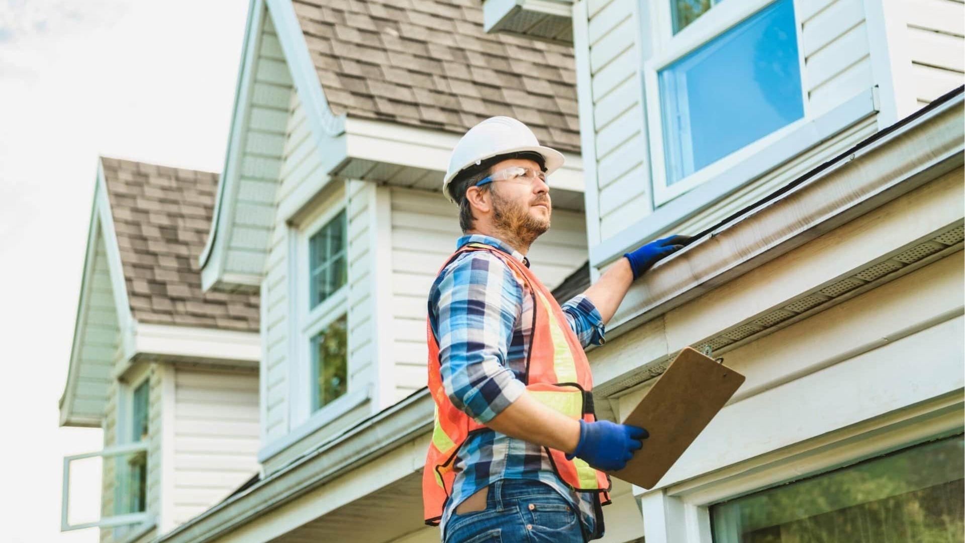Home inspector in hard hat and vest examining exterior of a house