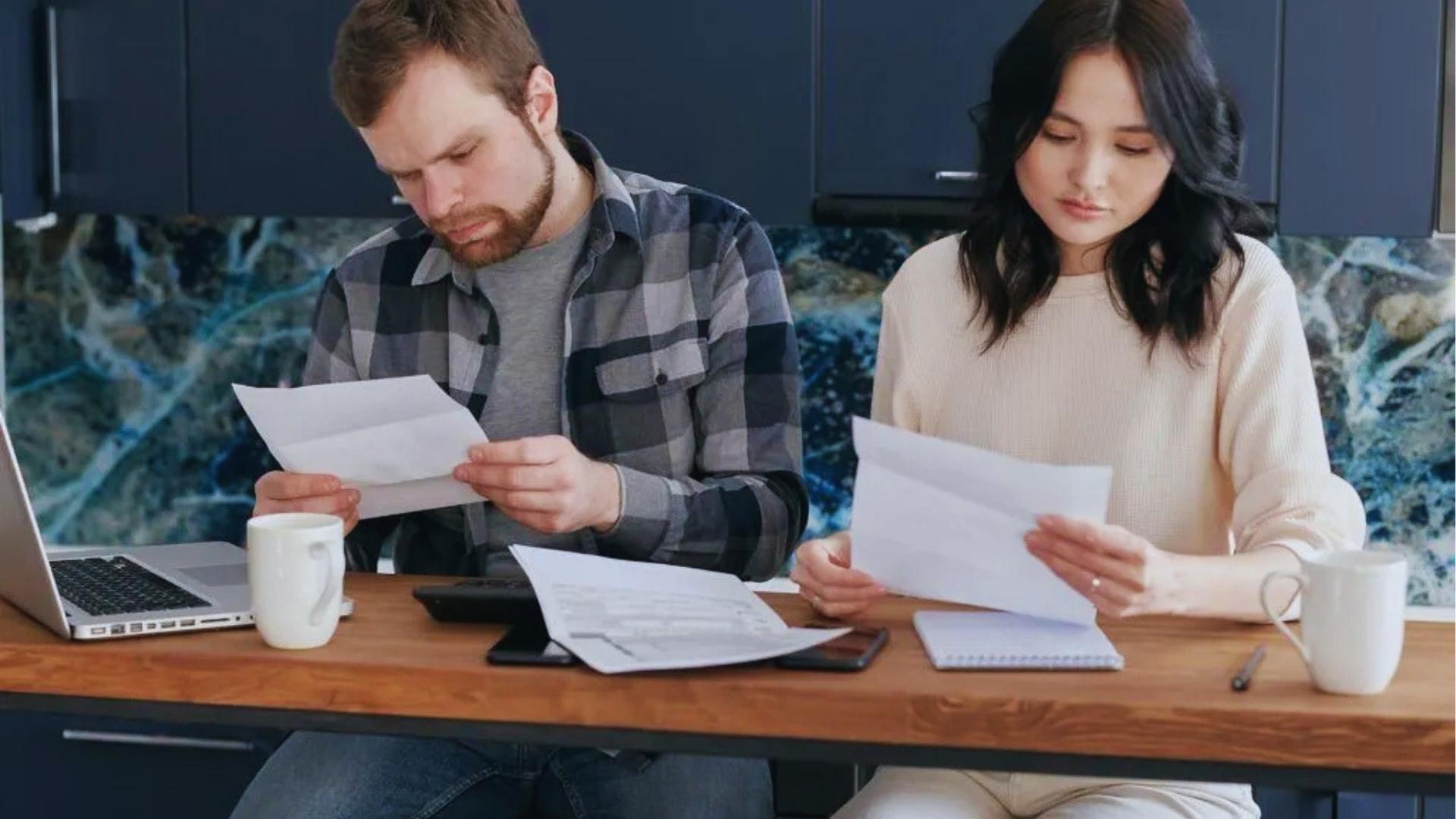 Worried couple reviewing mortgage foreclosure documents together at kitchen table with laptop and bills today.