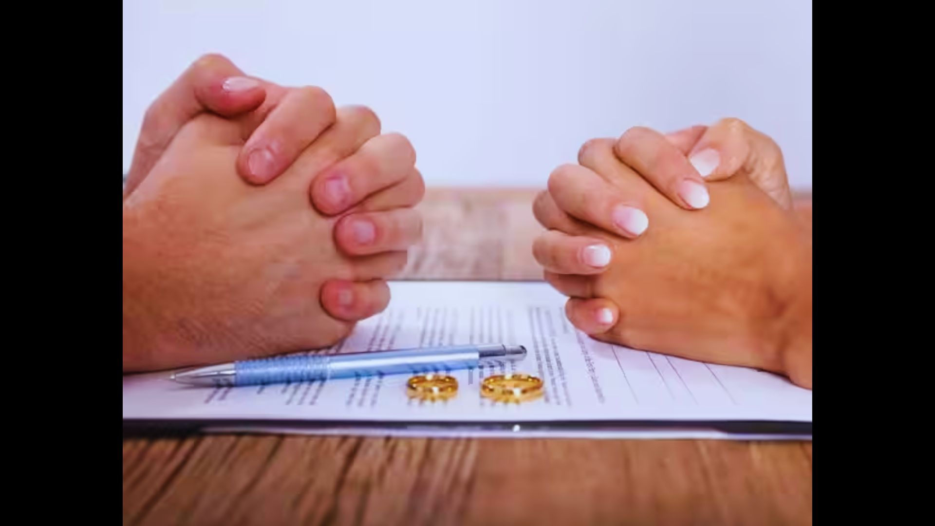 Two people holding hands over a legal document with two wedding rings and a pen on top.