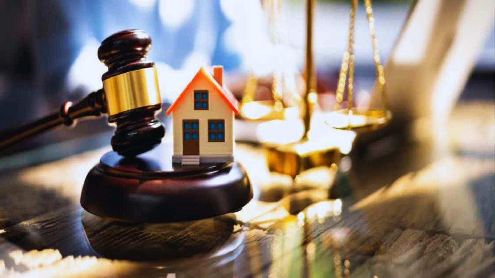 Judge gavel beside small model house on sounding block near golden justice scales symbolizing foreclosure.