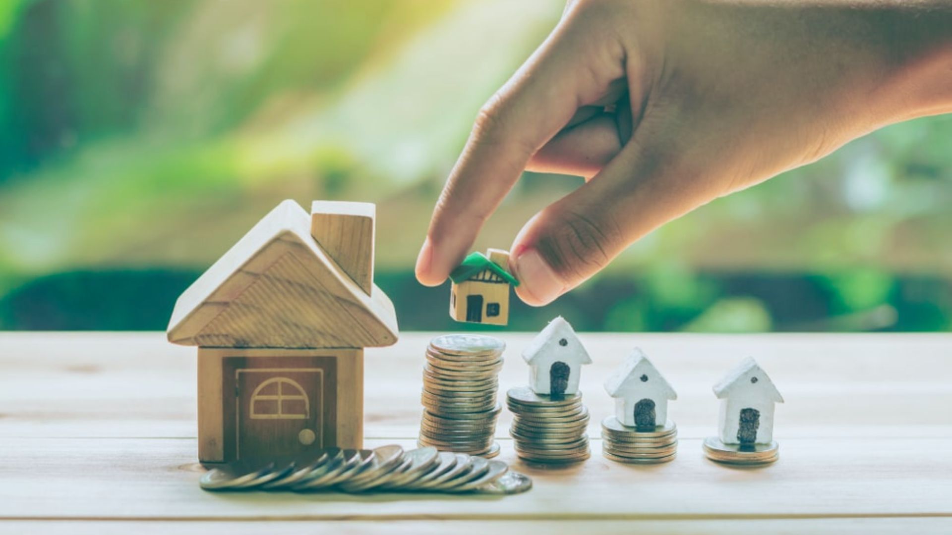 Real estate investment growth with house models on coin stacks and hand placing tiny house on coins