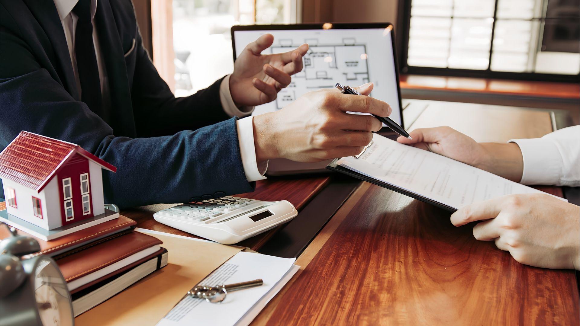 Agent explaining a property contract to a client with model house and calculator