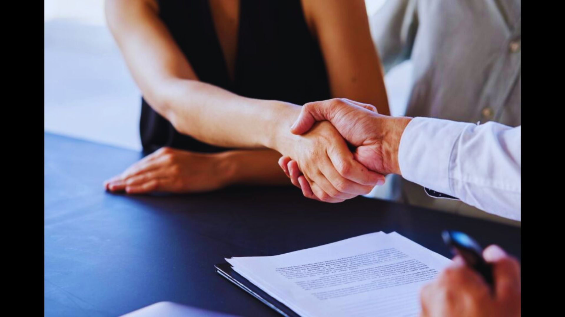 Two people shaking hands over legal papers on a desk.