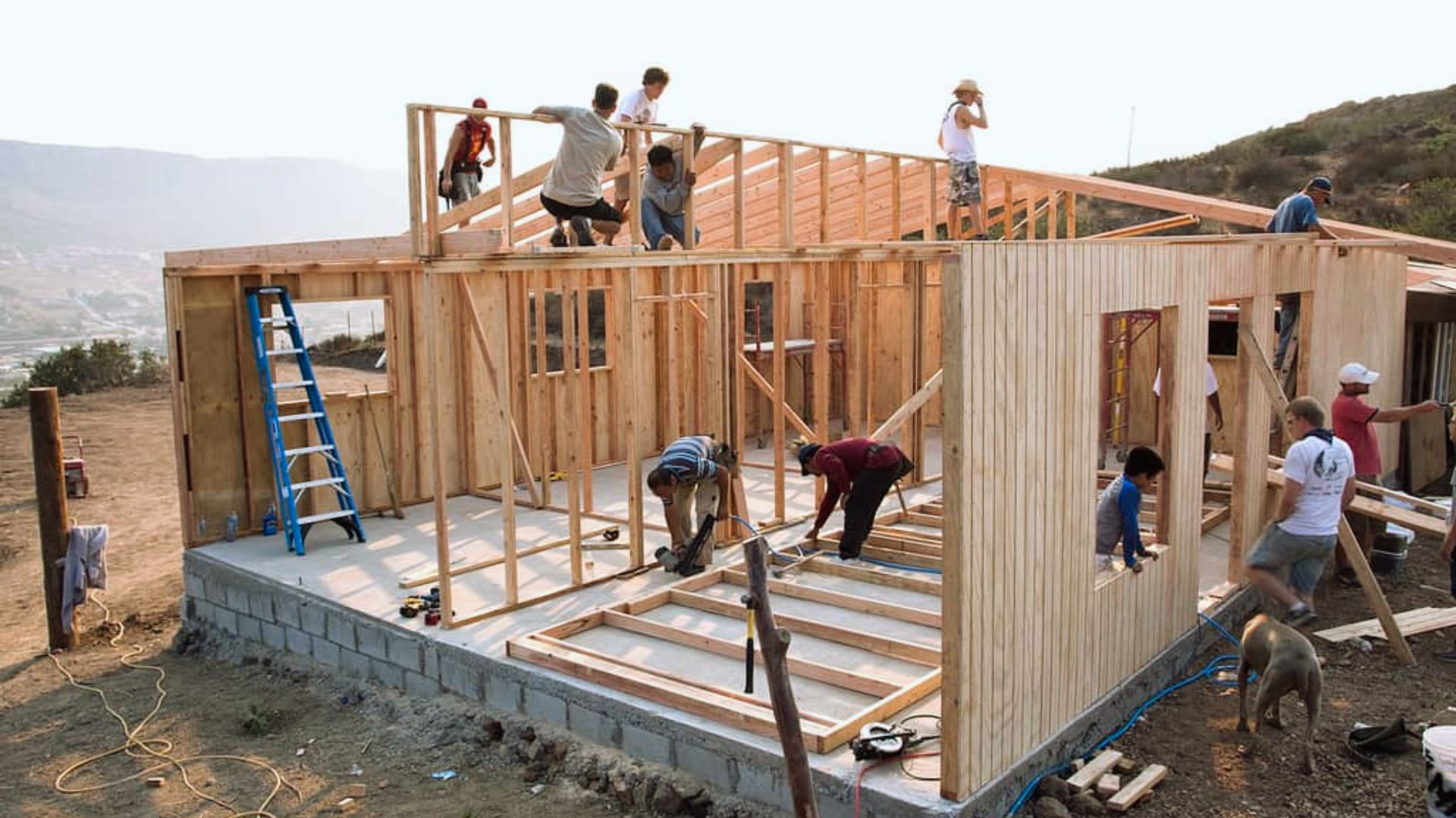 Volunteers framing wooden house under construction on concrete foundation, residential building project