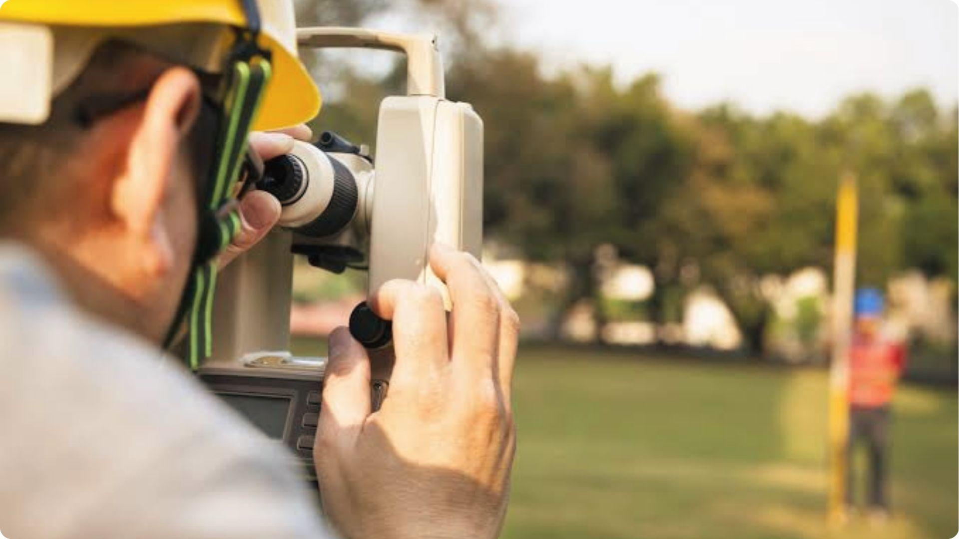 Surveyor peers through total station at distant pole marking property line during boundary survey