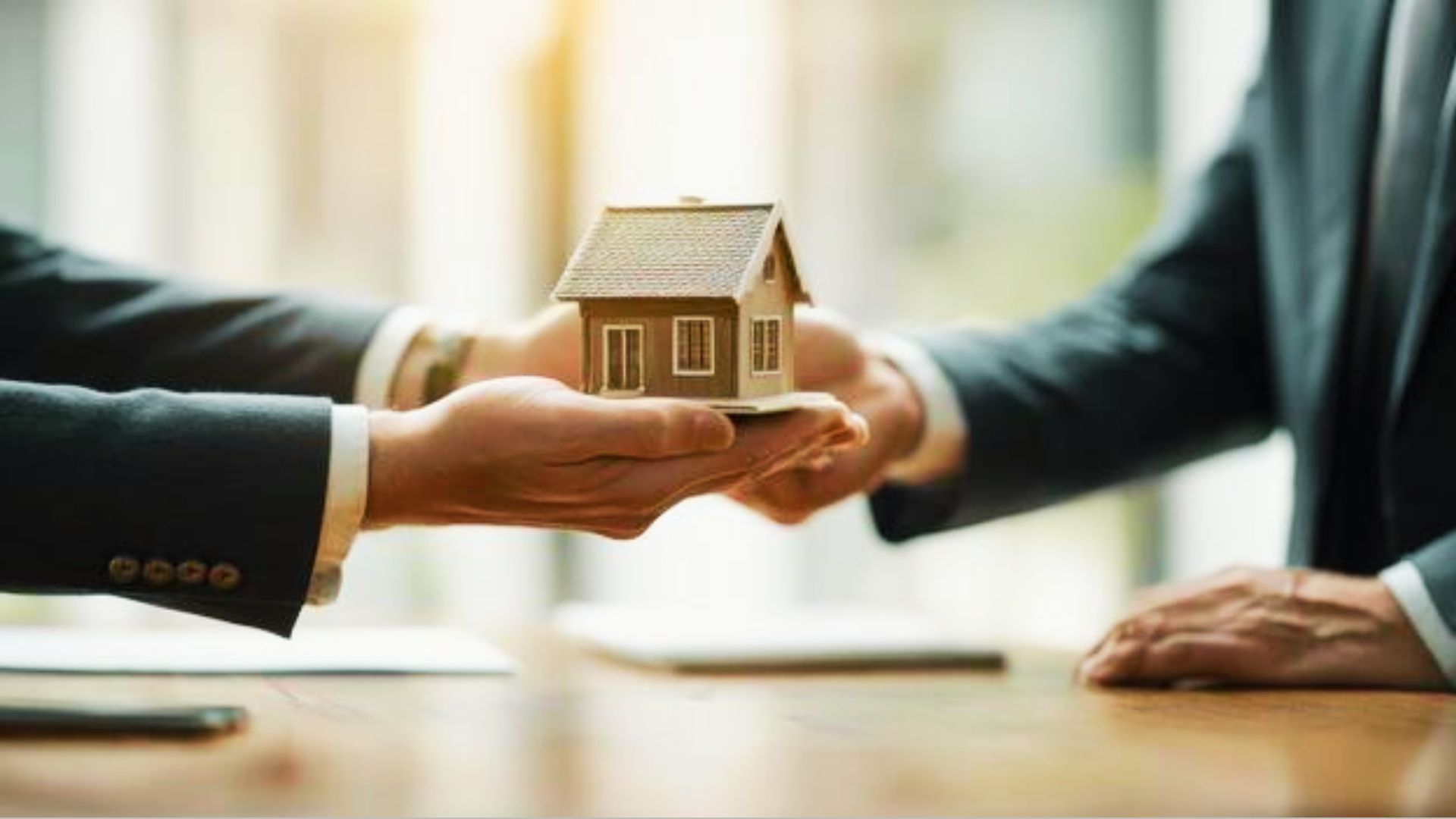 A businessman hands a house model to a real estate agent, the concept of community property trusts in real estate.