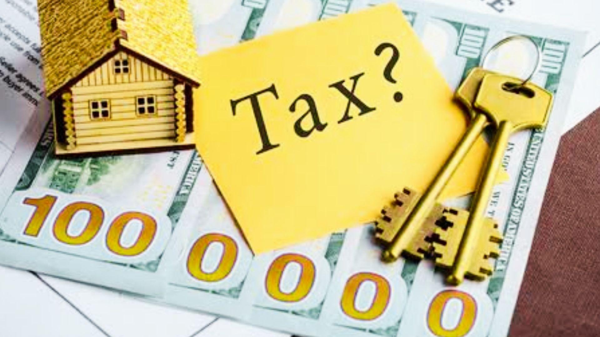 Magnifying glass over miniature house models beside property taxes paper, dollar bills, and calculators.
