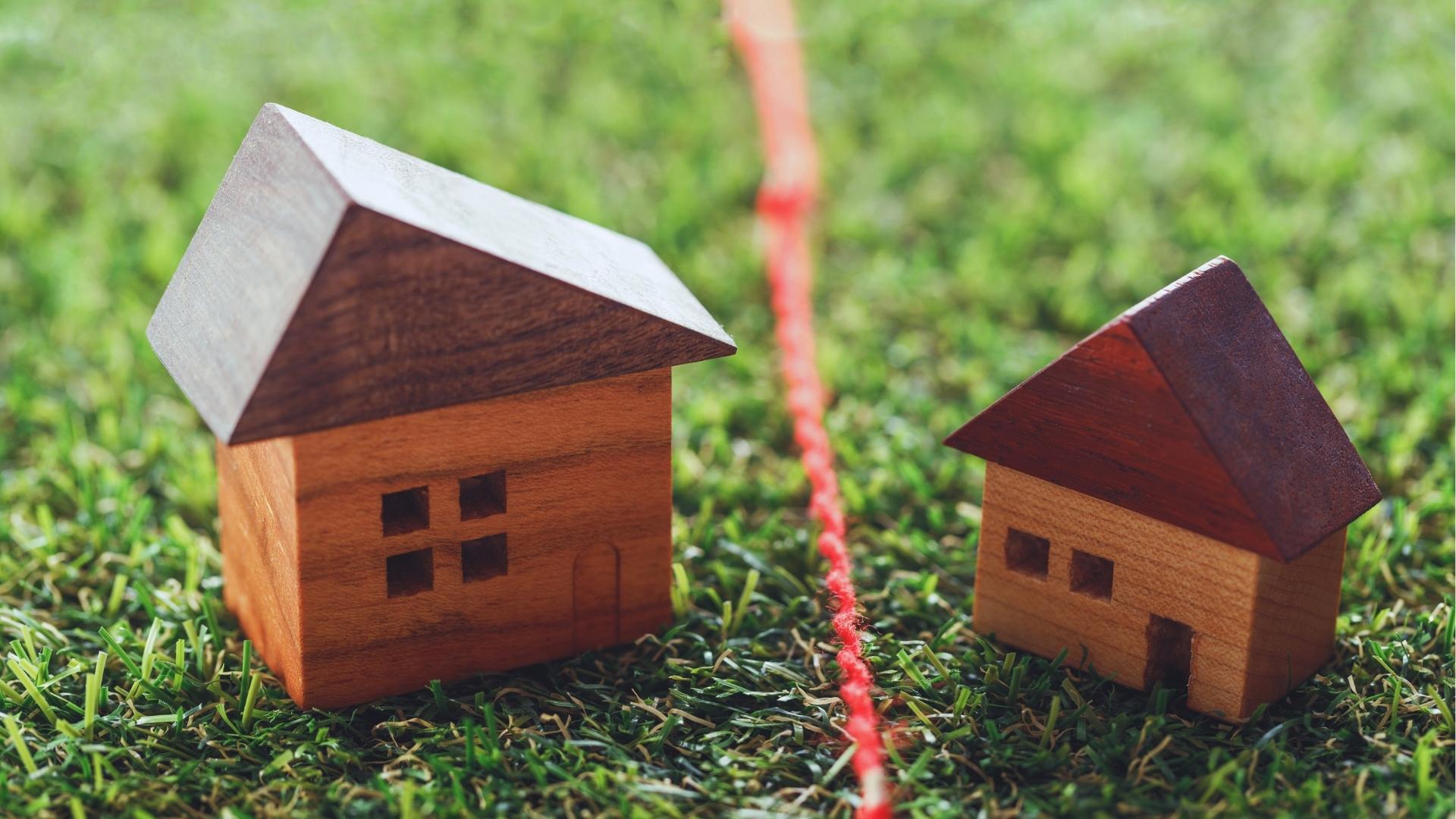 Two small wooden model houses separated by red string marking property line boundary on grass.