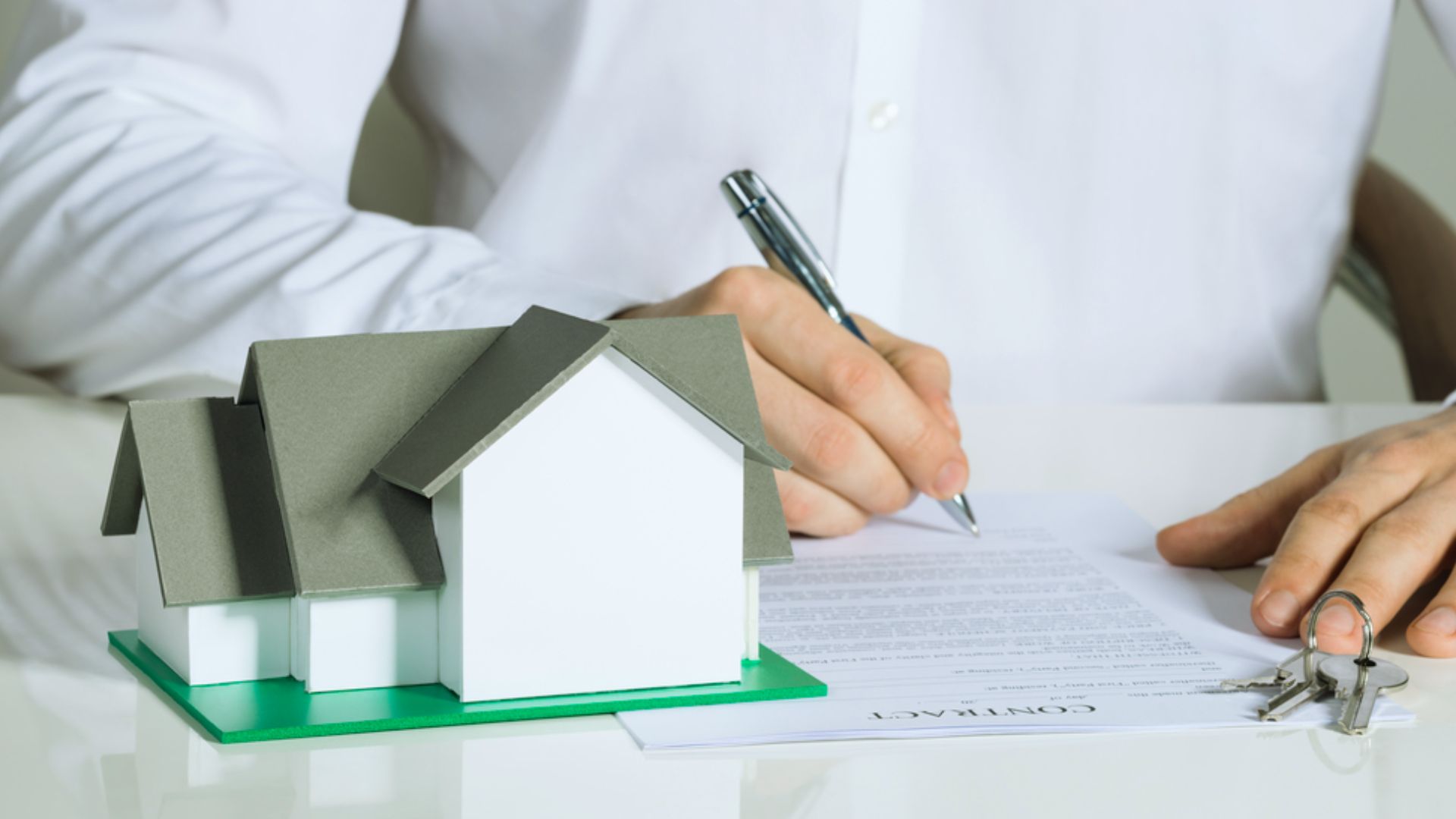 Person signing quitclaim deed property contract with gray model house and house keys