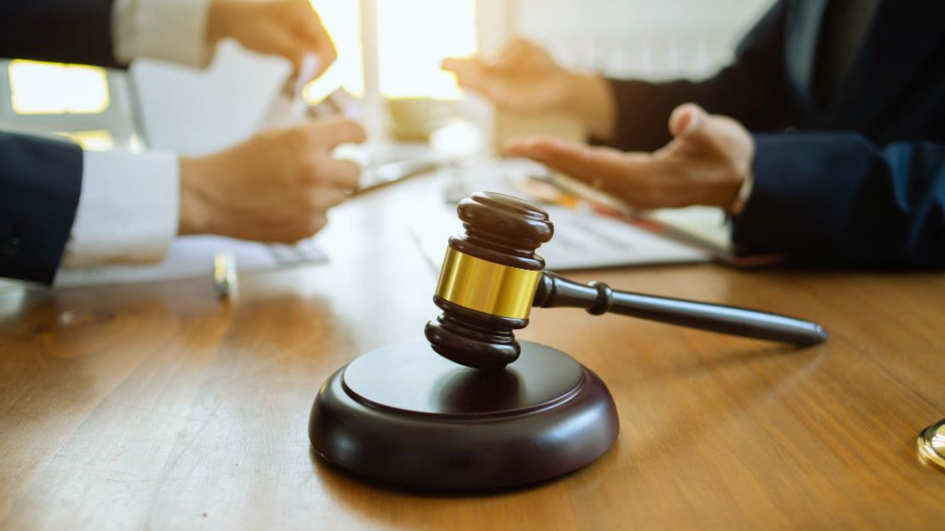 Legal consultation with judge gavel on desk, lawyers discussing case documents in background