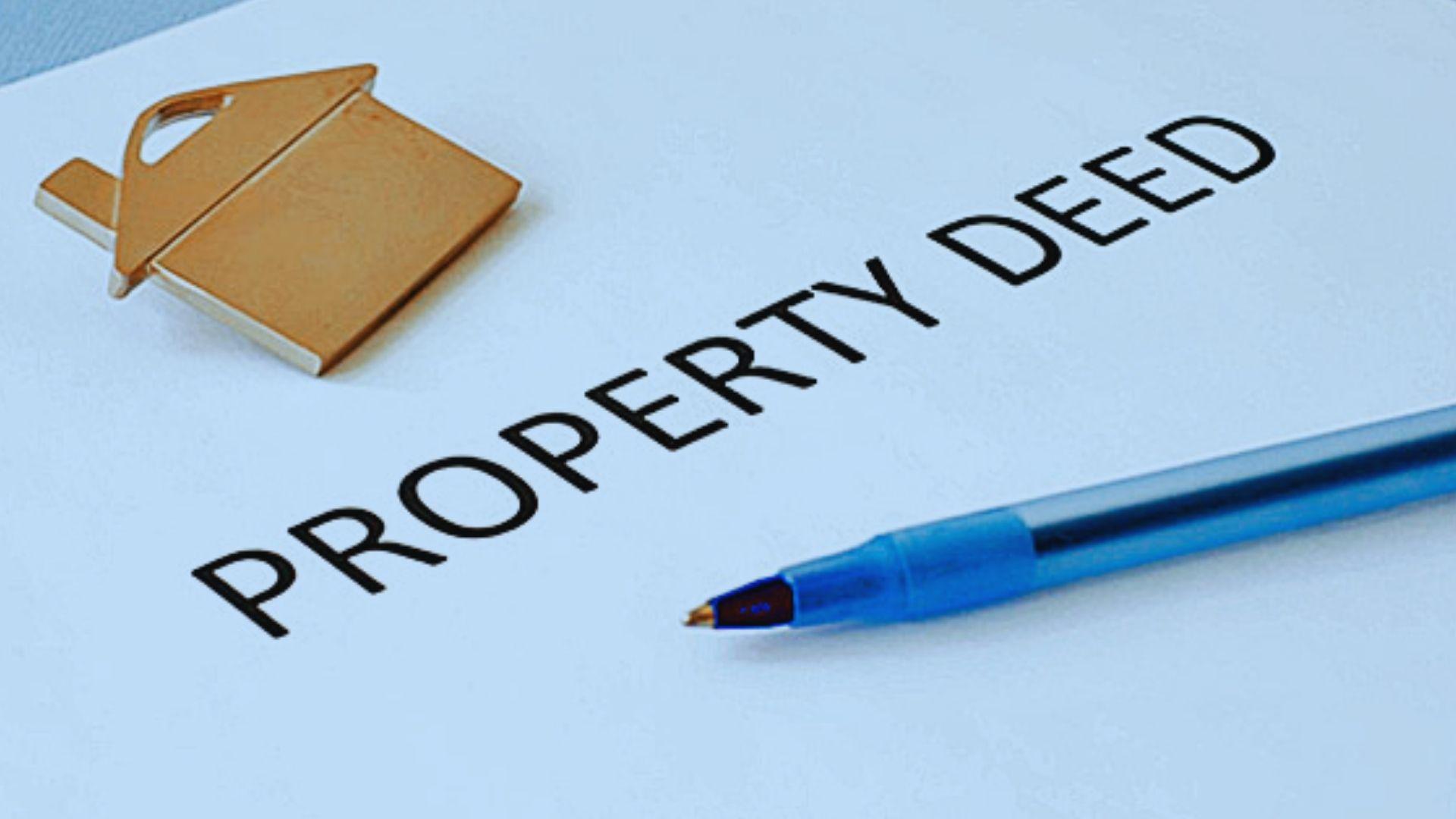 Gold house-shaped keychain and blue pen resting on paper titled PROPERTY DEED.