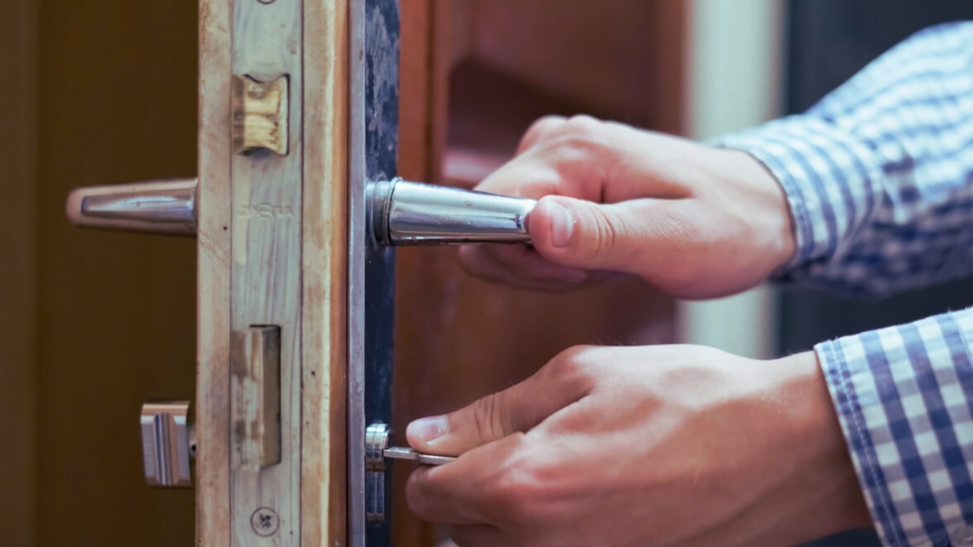 Close-up of a person's hand inserting a key to unlock a wooden door lock.
