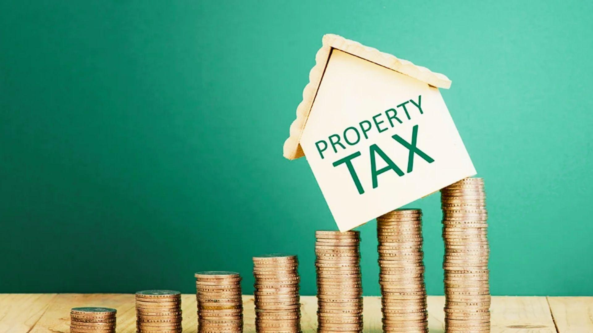 House-shaped PROPERTY TAX sign balancing on ascending stacks of coins against green background.