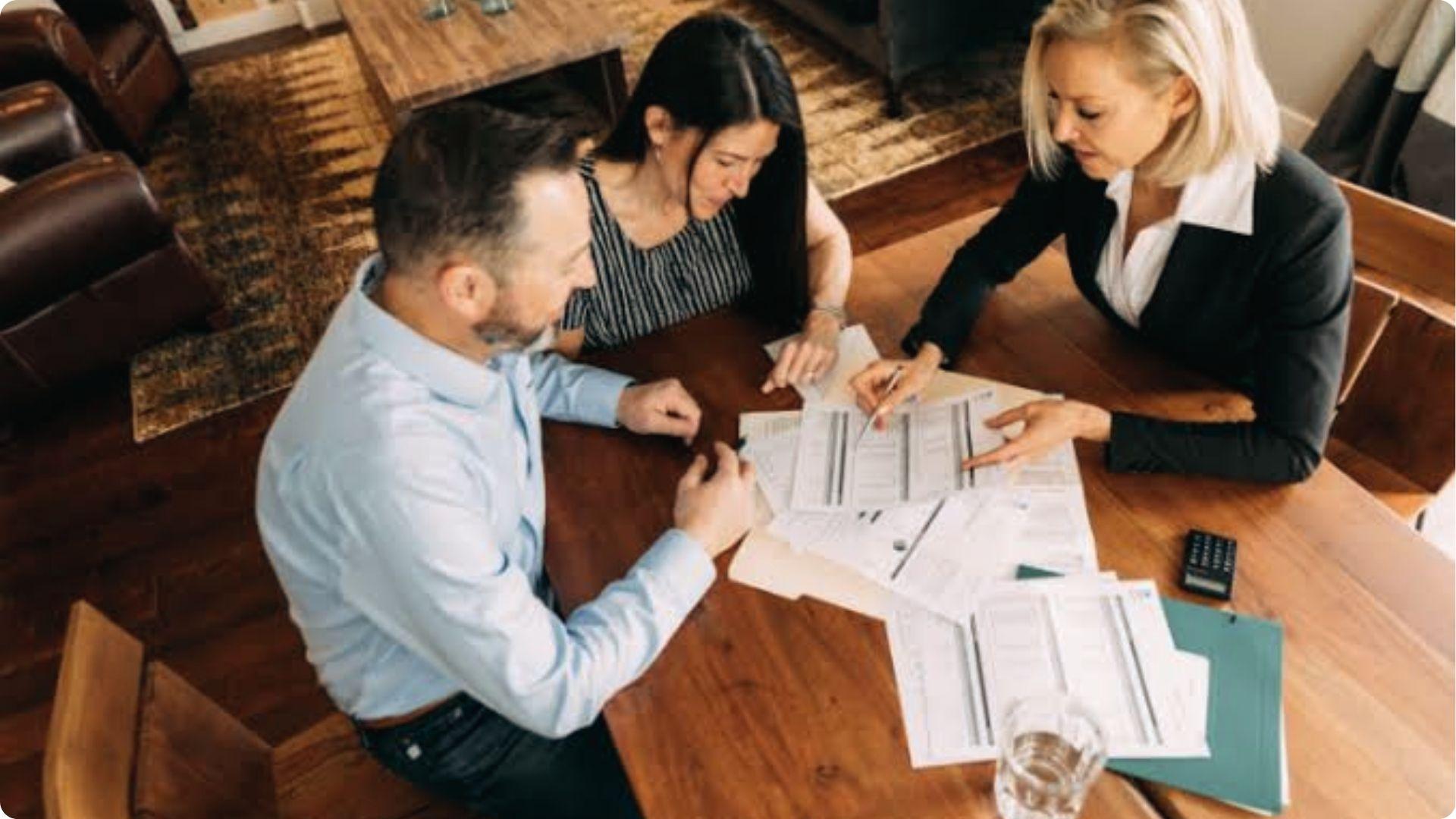 Executor represents property details, agent explaining financial documents to couple at table.