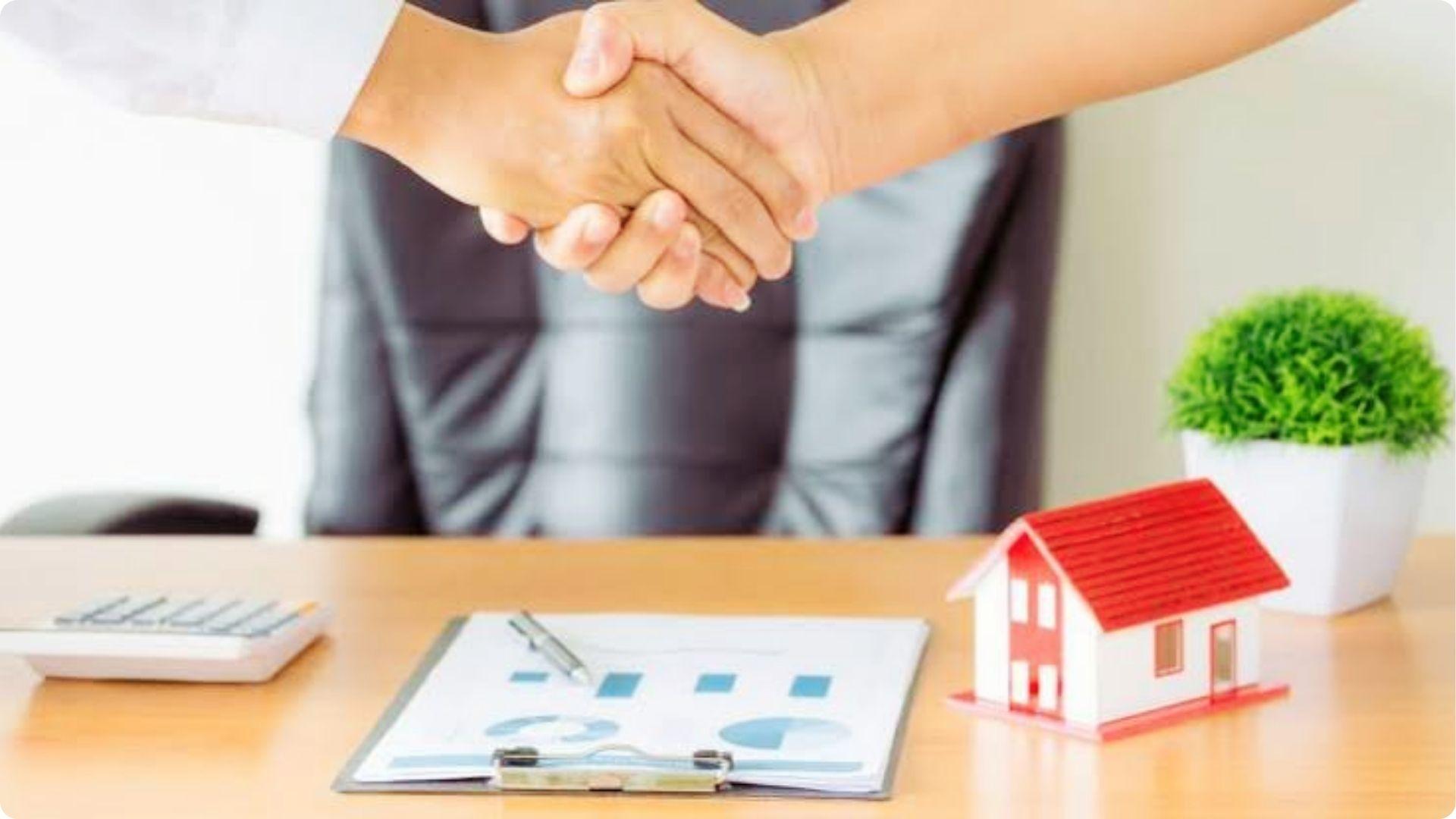 Handshake closing property deed transfer deal with house model and financial charts on desk
