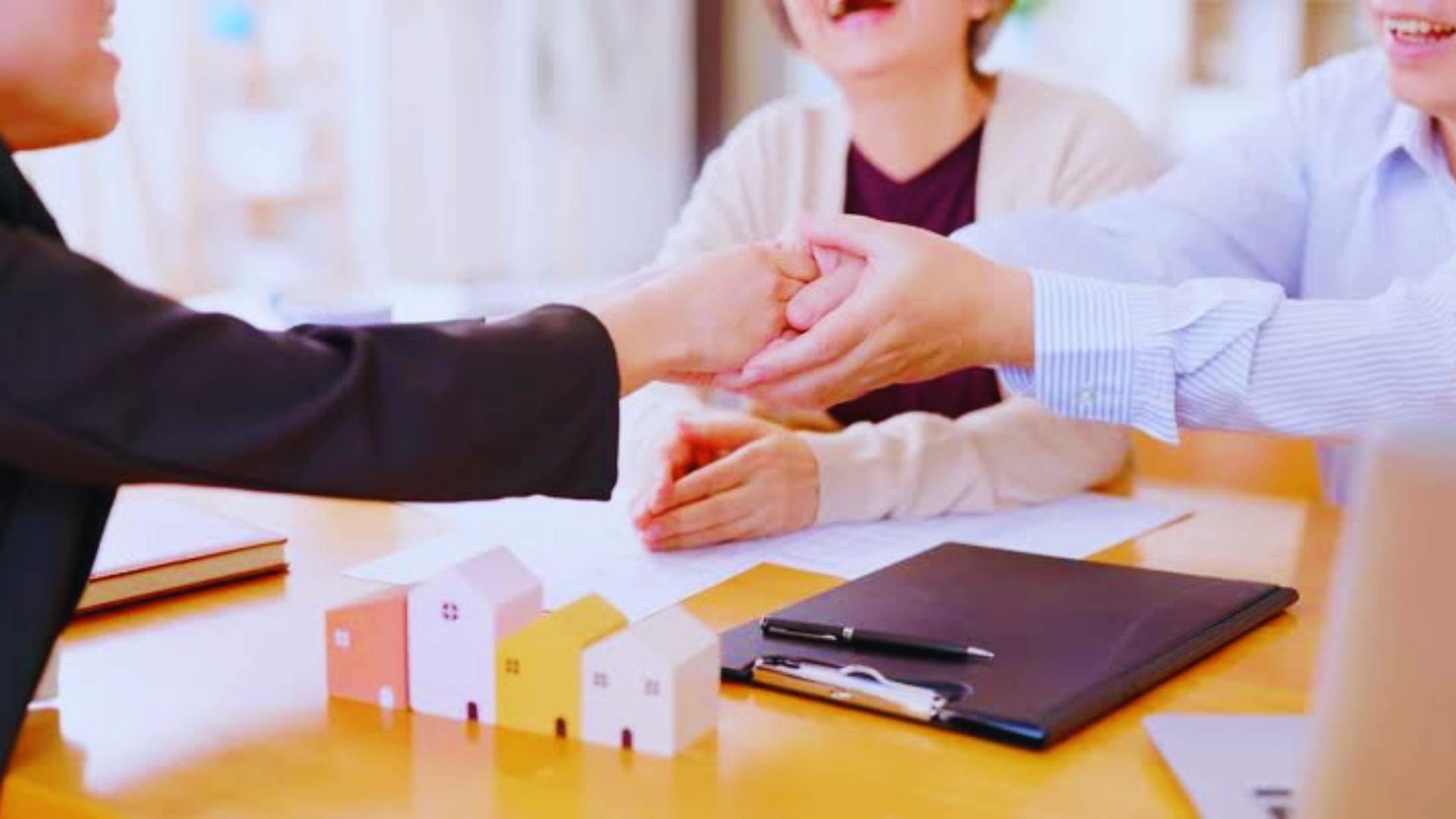 A handshake between two people at a table, accompanied by a house model, representing a community property trust concept.