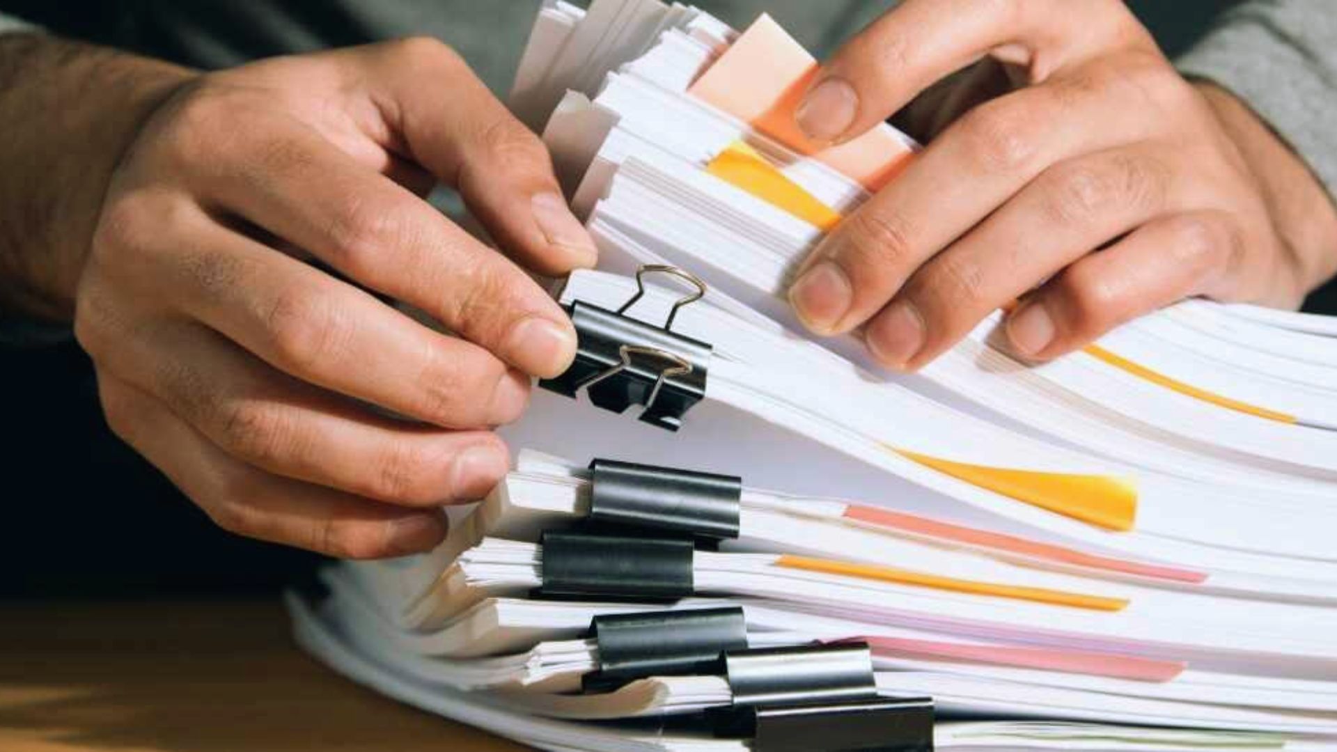 Hands organizing large stack of legal documents with binder clips and sticky tabs, paperwork review