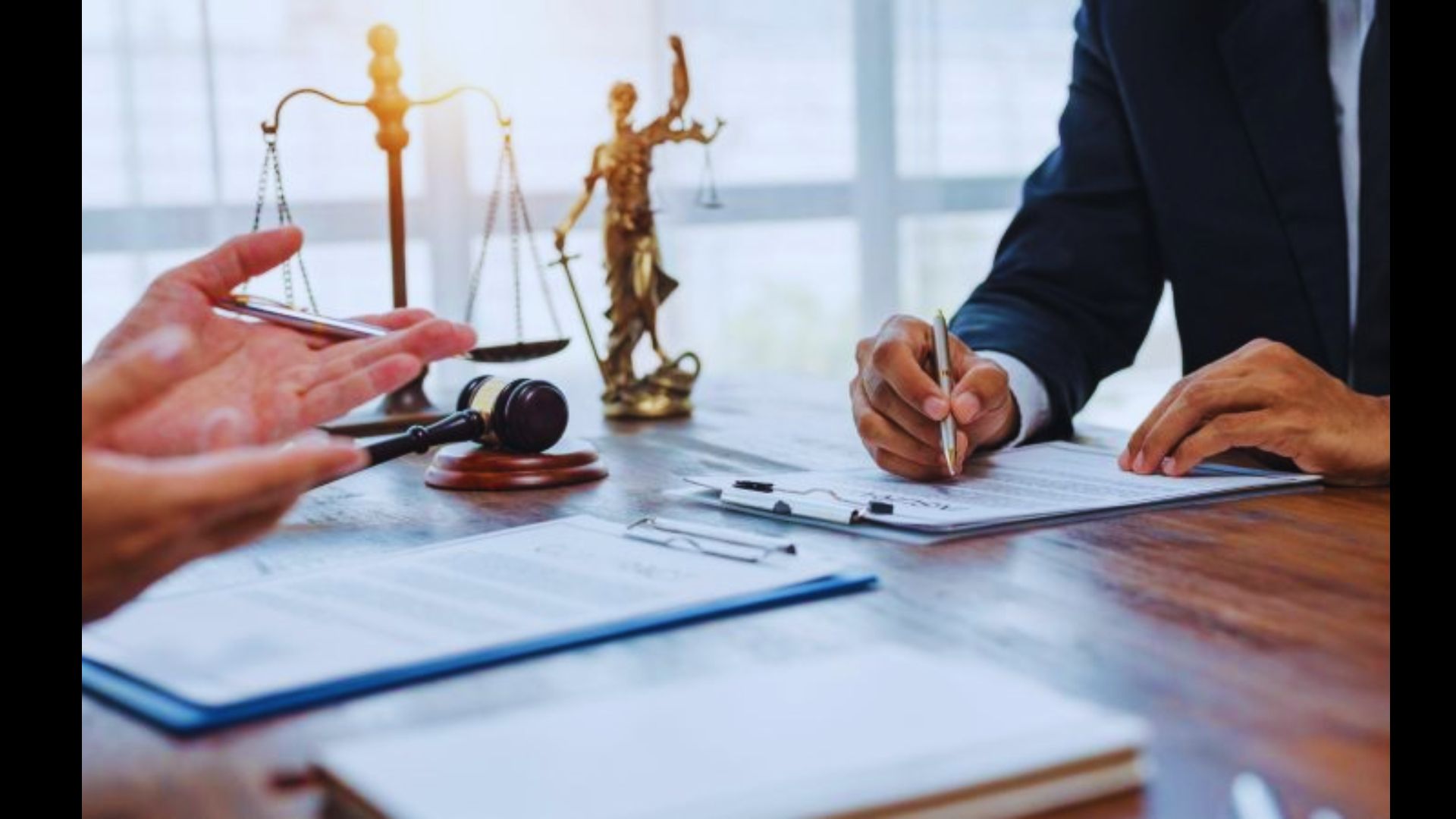 Person signing legal document at a desk with scales of Lady Justice in background.