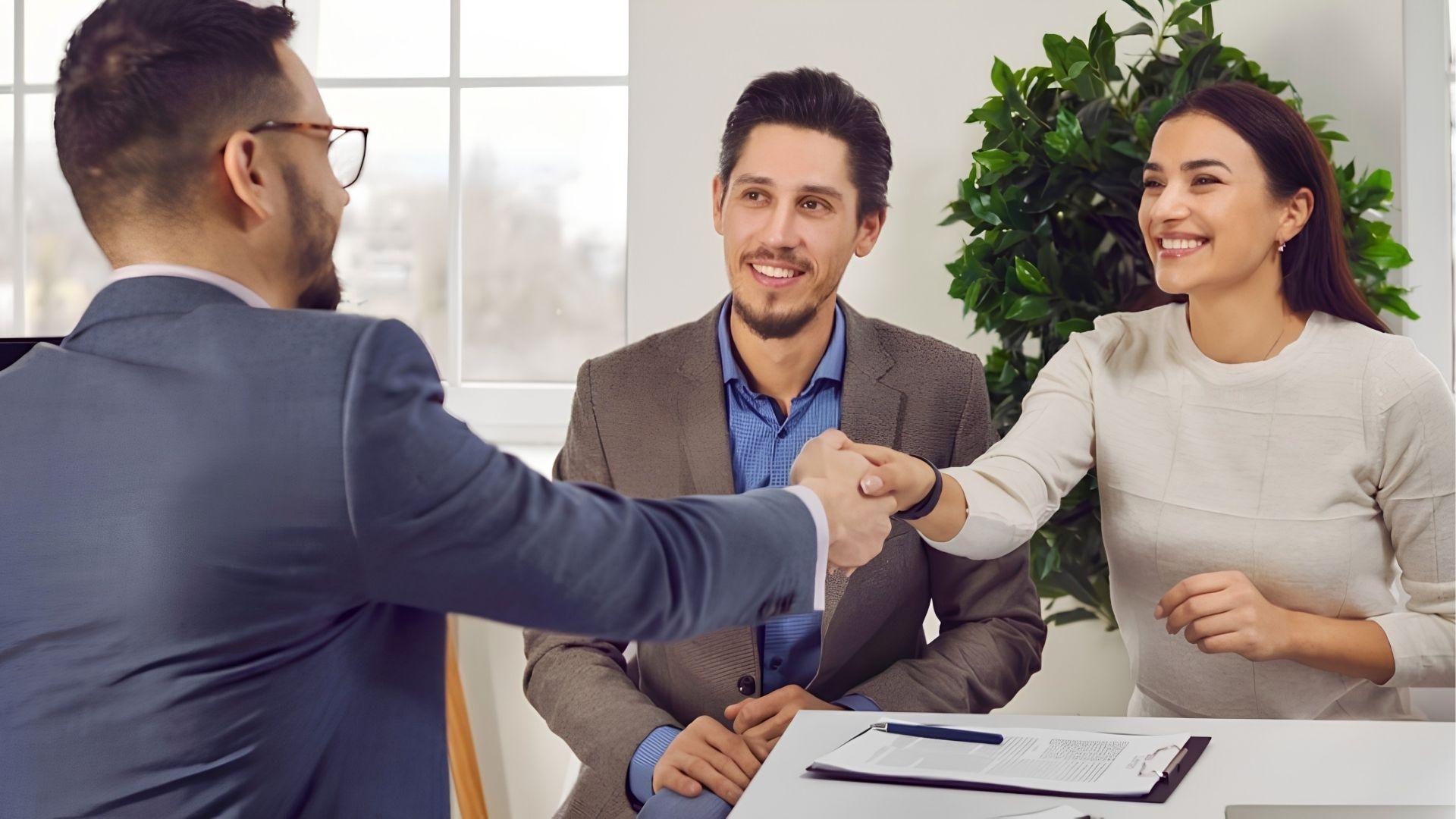 Happy homebuyers shaking hands with real estate agent after property agreement.