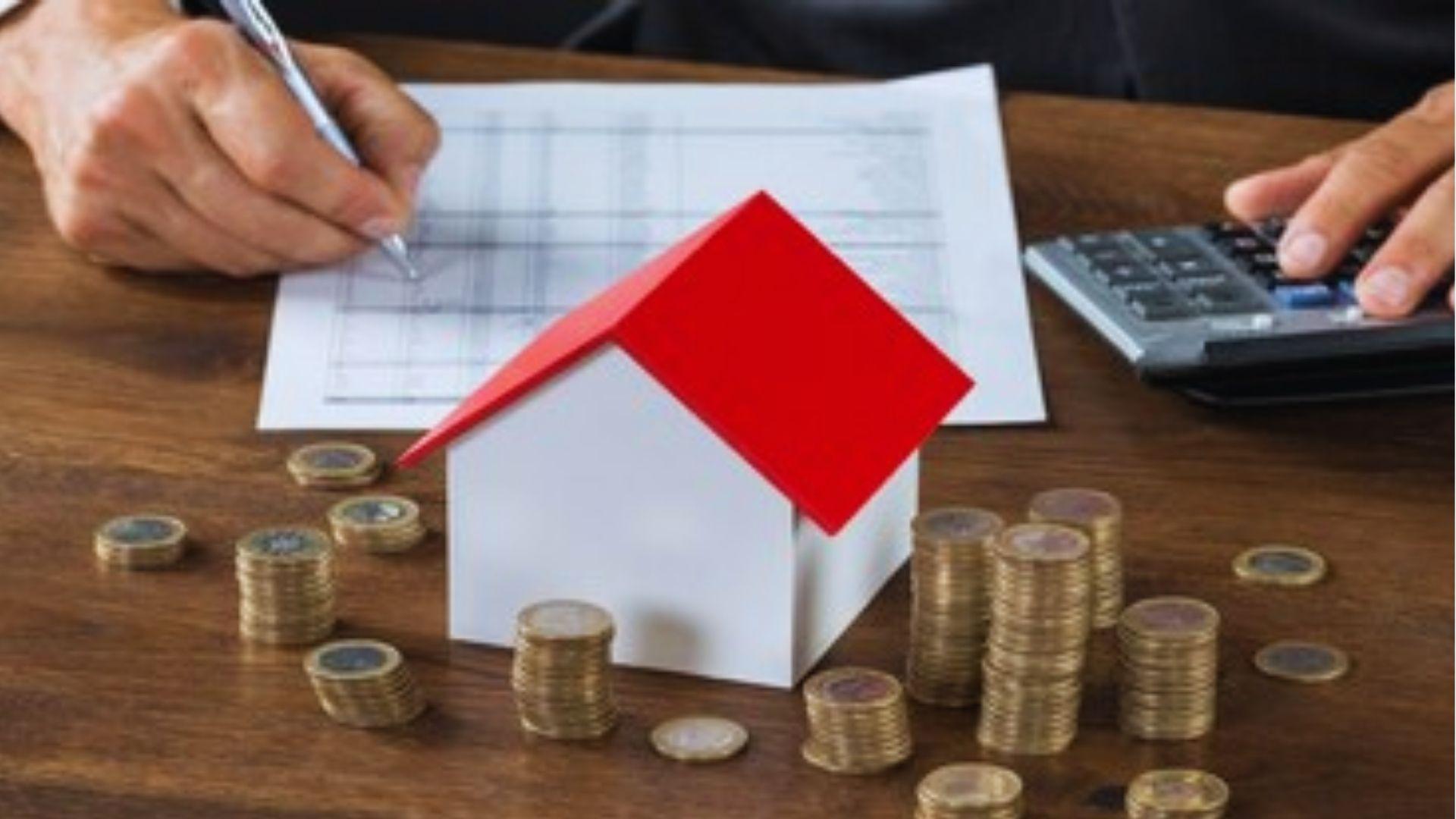 White paper model house with red roof surrounded by stacks of coins